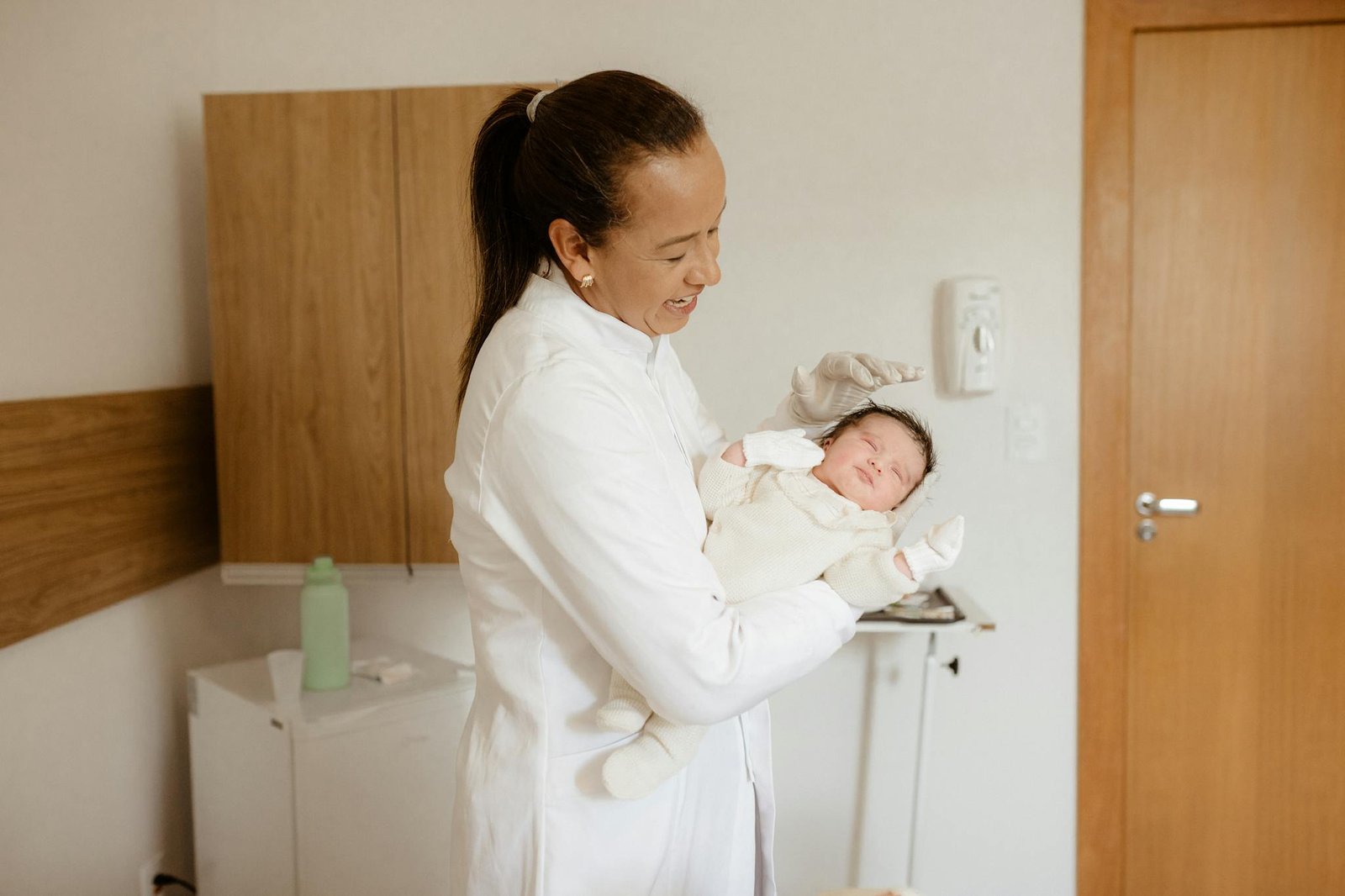 A medical practitioner gently holding a newborn baby in a hospital room, symbolizing care and health.