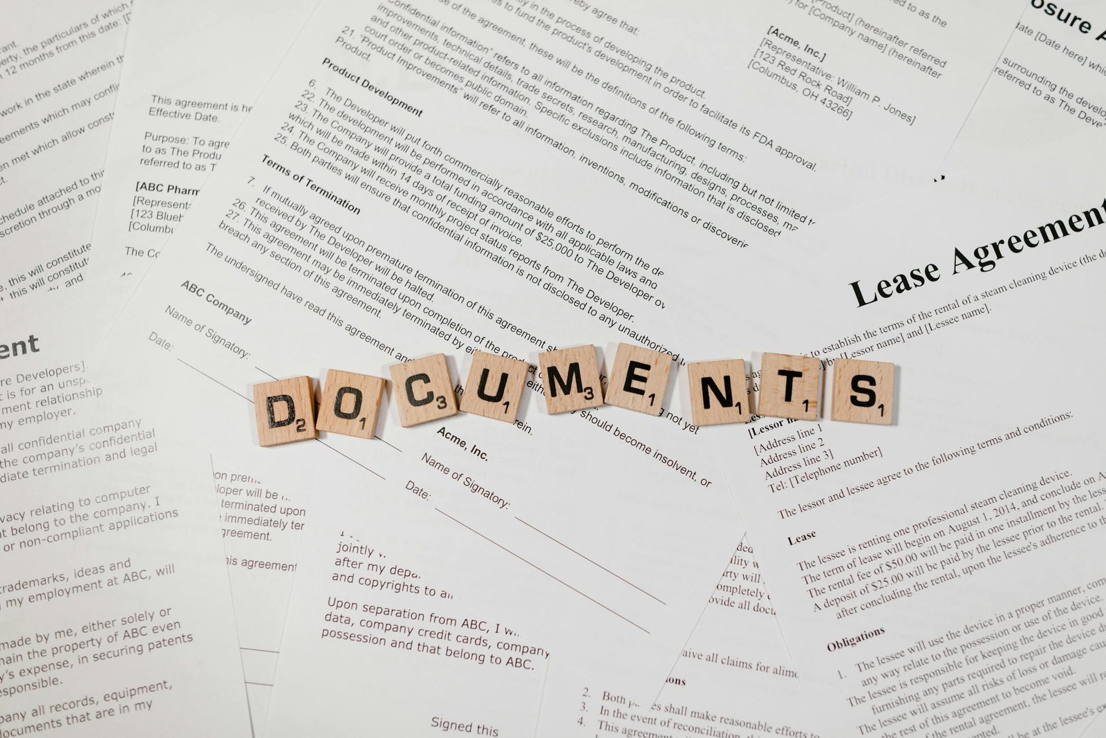 Top view of scrabble tiles spelling 'DOCUMENTS' on various contracts and agreements.
